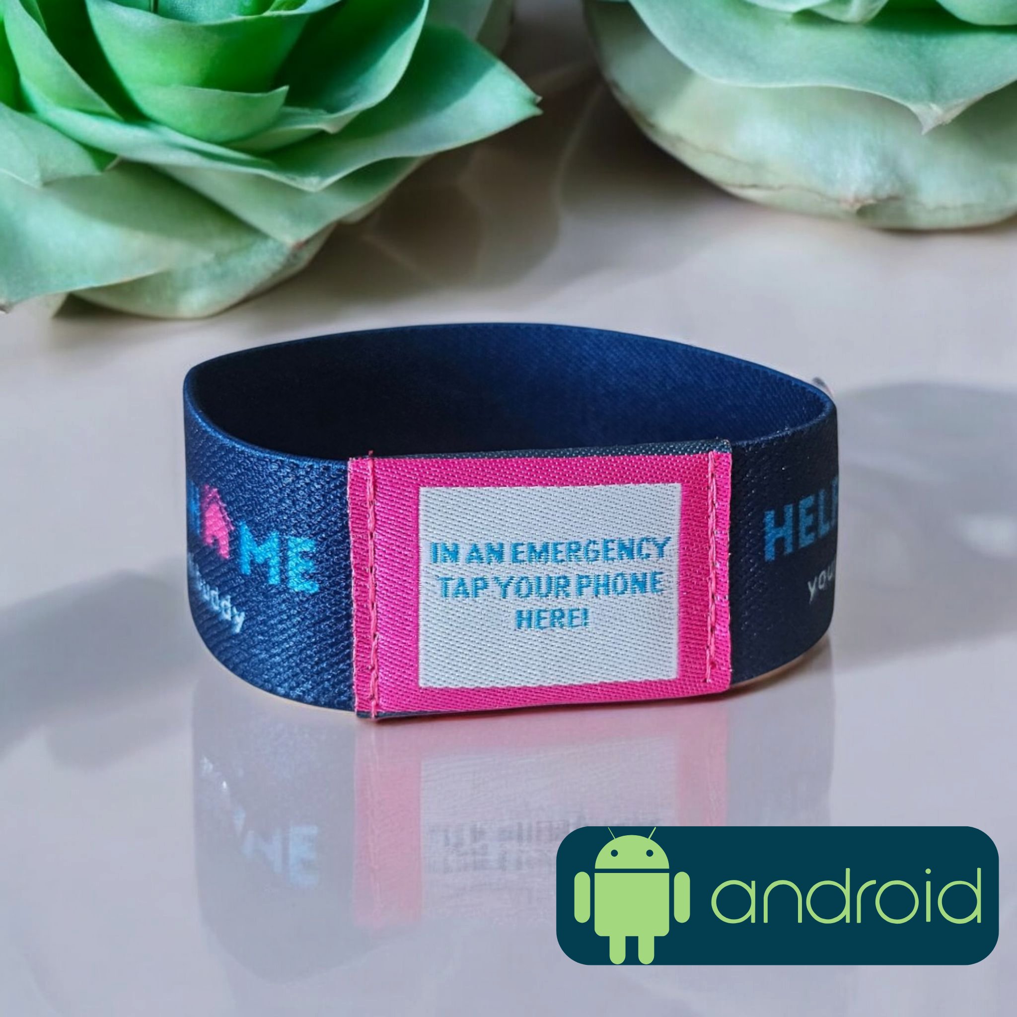 Navy blue and pink emergency wristband with Android logo on a reflective surface with flowers in the background